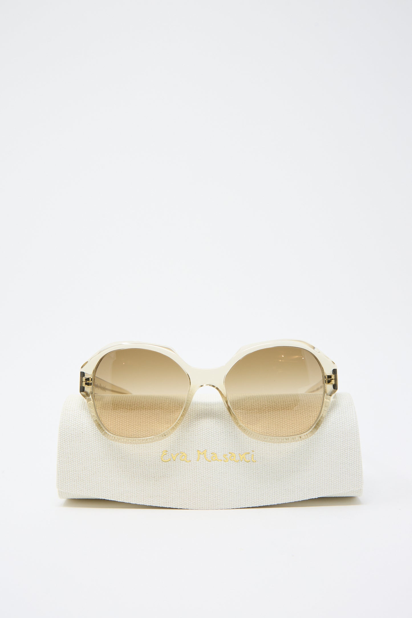 A pair of 001 Sunglasses in Toast with an oversized hexagonal frame and gradient Zeiss lenses displayed on a white fabric case labeled "Eva Masaki.