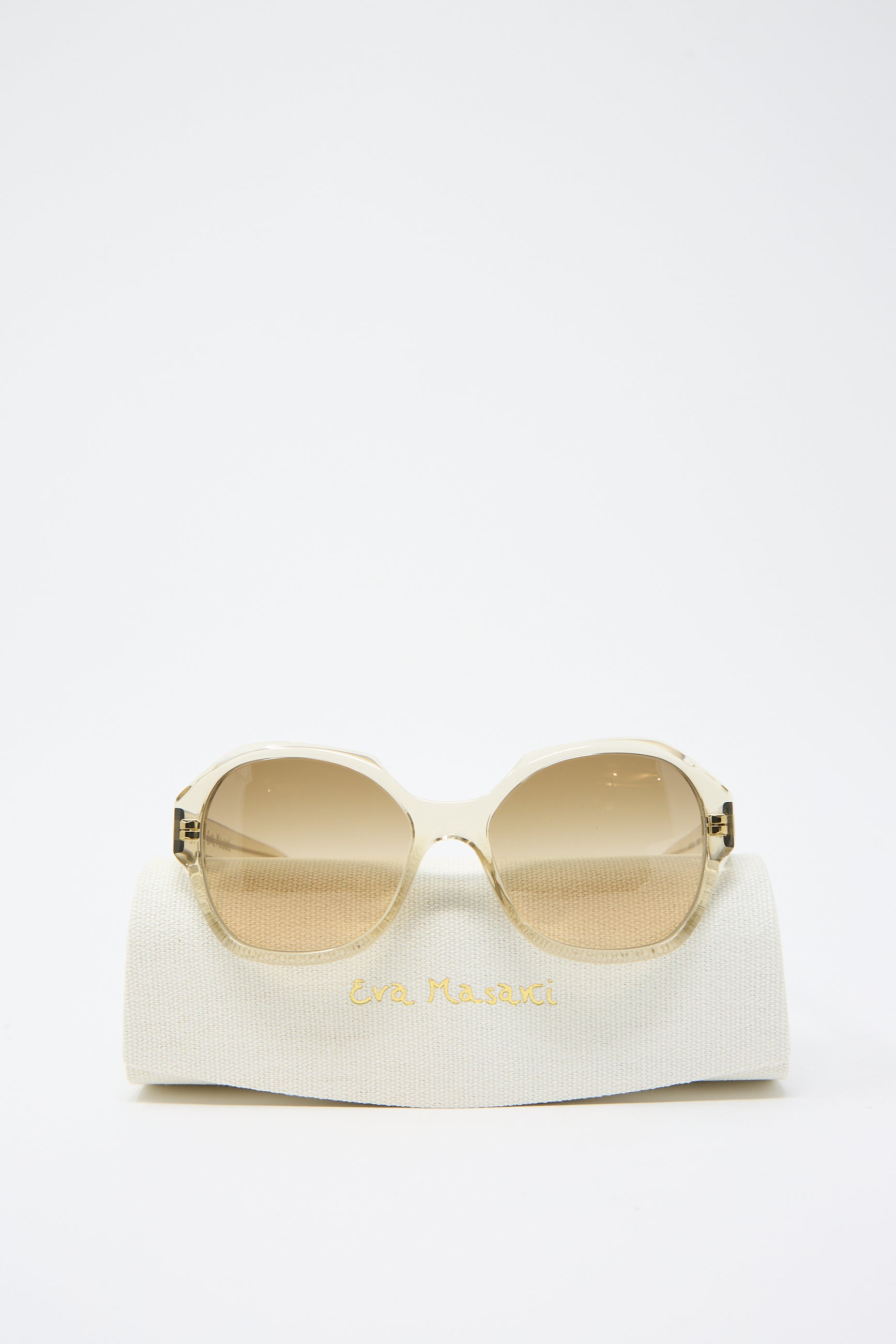 A pair of 001 Sunglasses in Toast with an oversized hexagonal frame and gradient Zeiss lenses displayed on a white fabric case labeled "Eva Masaki.