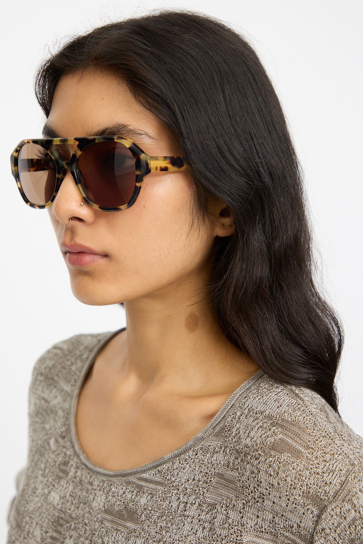 A woman with long dark hair wears Eva Masaki Chiyo Aviator Sunglasses in Tokyo and a textured beige top, looking to the side against a plain background.
