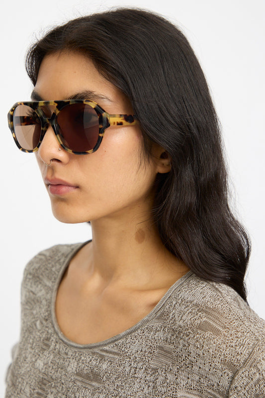 A woman with long dark hair wears Eva Masaki Chiyo Aviator Sunglasses in Tokyo and a textured beige top, looking to the side against a plain background.