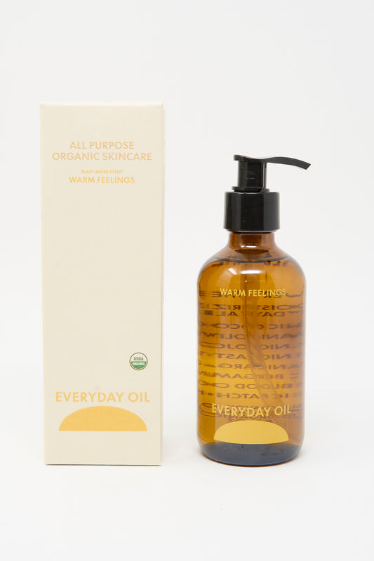 A bottle of Everyday Oil’s Warm Feelings - 8 Ounces, an organic body oil with a pump dispenser, is displayed beside its box labeled “All Purpose Organic Skincare” on a white background.