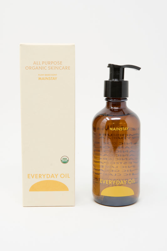 An 8-ounce bottle of Everyday Oil’s Mainstay Blend with a pump stands beside its "All Purpose Organic Skincare" box, both featuring a minimalist beige and yellow design.
