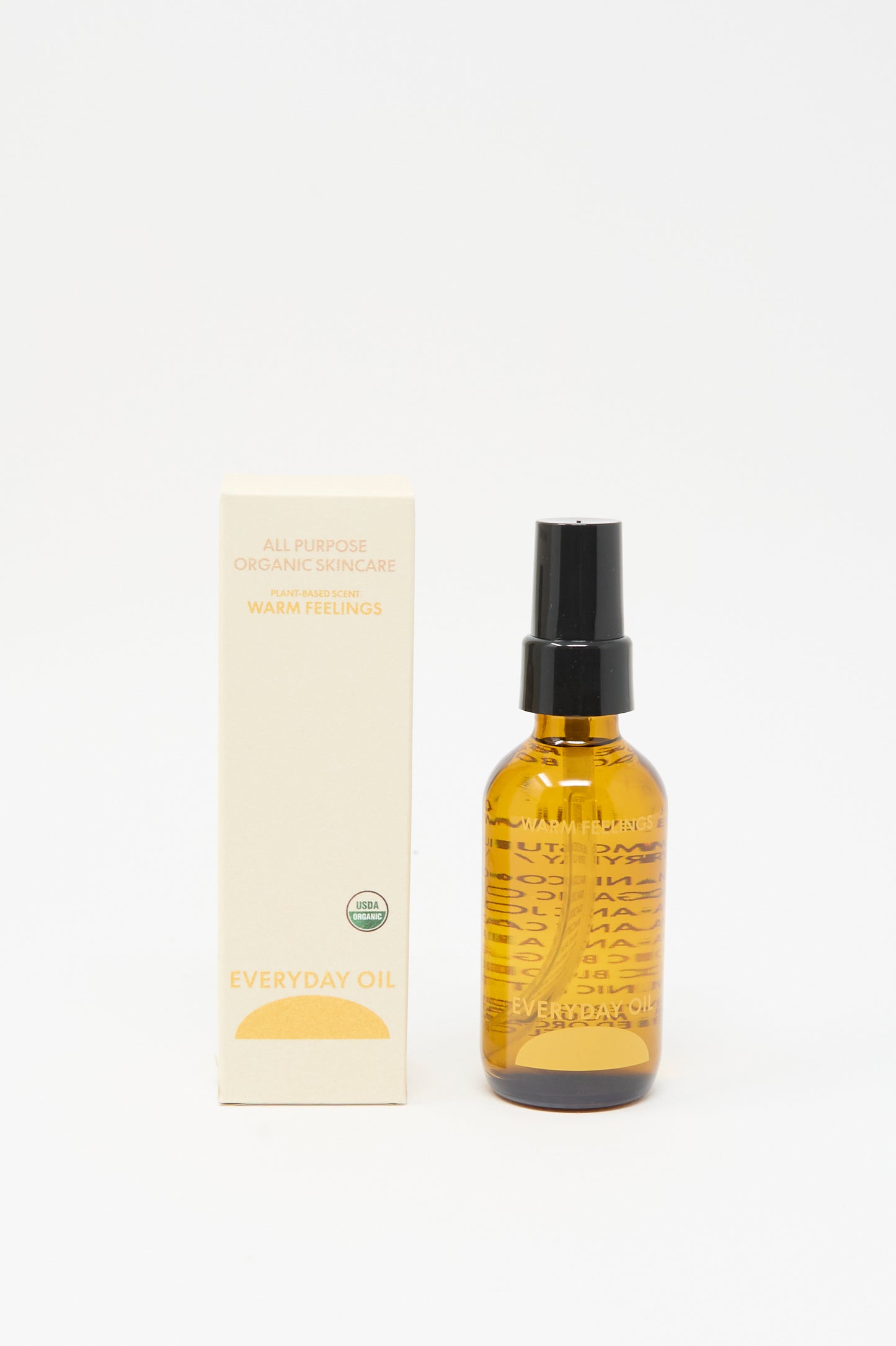A 2-ounce bottle of Everyday Oil Warm Feelings with a black pump stands by its beige "All Purpose Organic Skincare" box, showcasing this microbiome-friendly organic body oil against a white background.