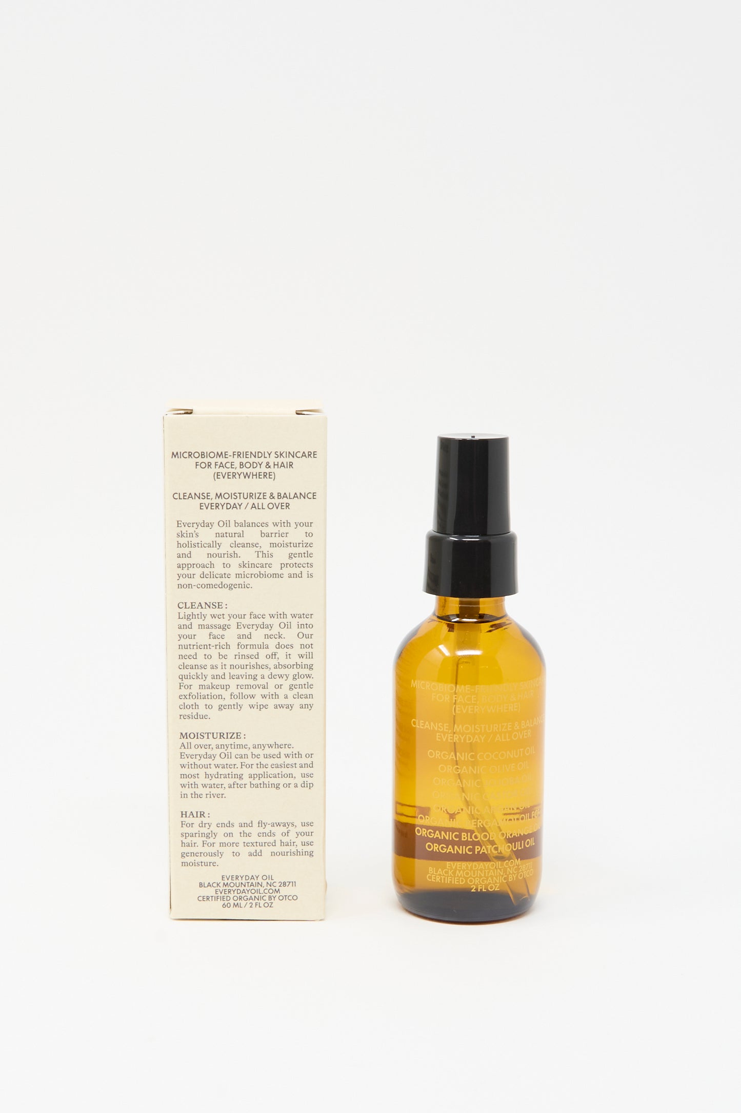 Amber pump bottle of Everyday Oil's Warm Feelings (2 Ounces) with labeled product info stands beside a beige box detailing usage and ingredients, both upright on a white background—highlighting this microbiome-friendly organic body oil.