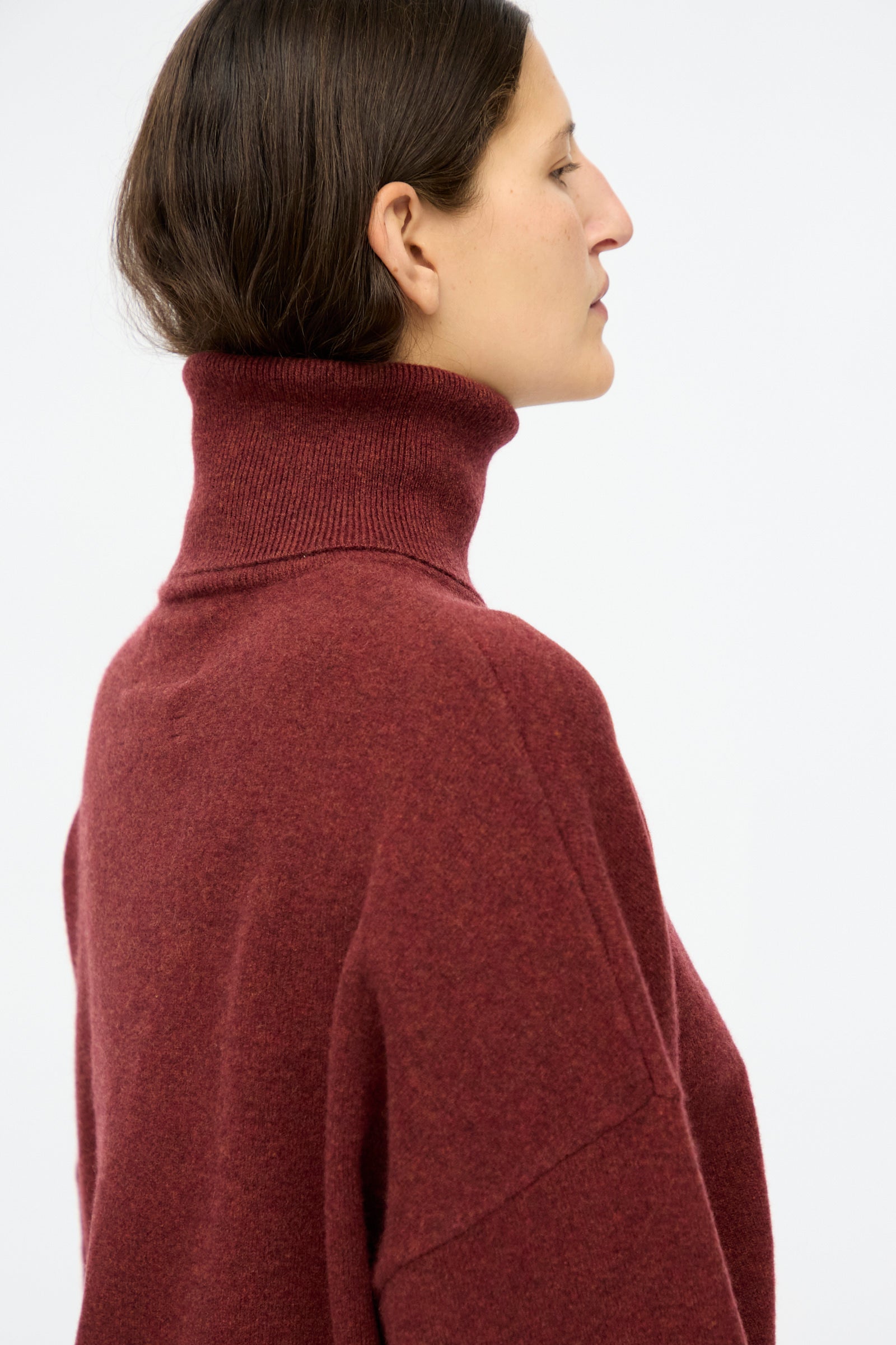 A person in profile wears the Extreme Cashmere No. 204 Jill Sweater in Maroon, a relaxed-fit cashmere turtleneck, against a plain light background.