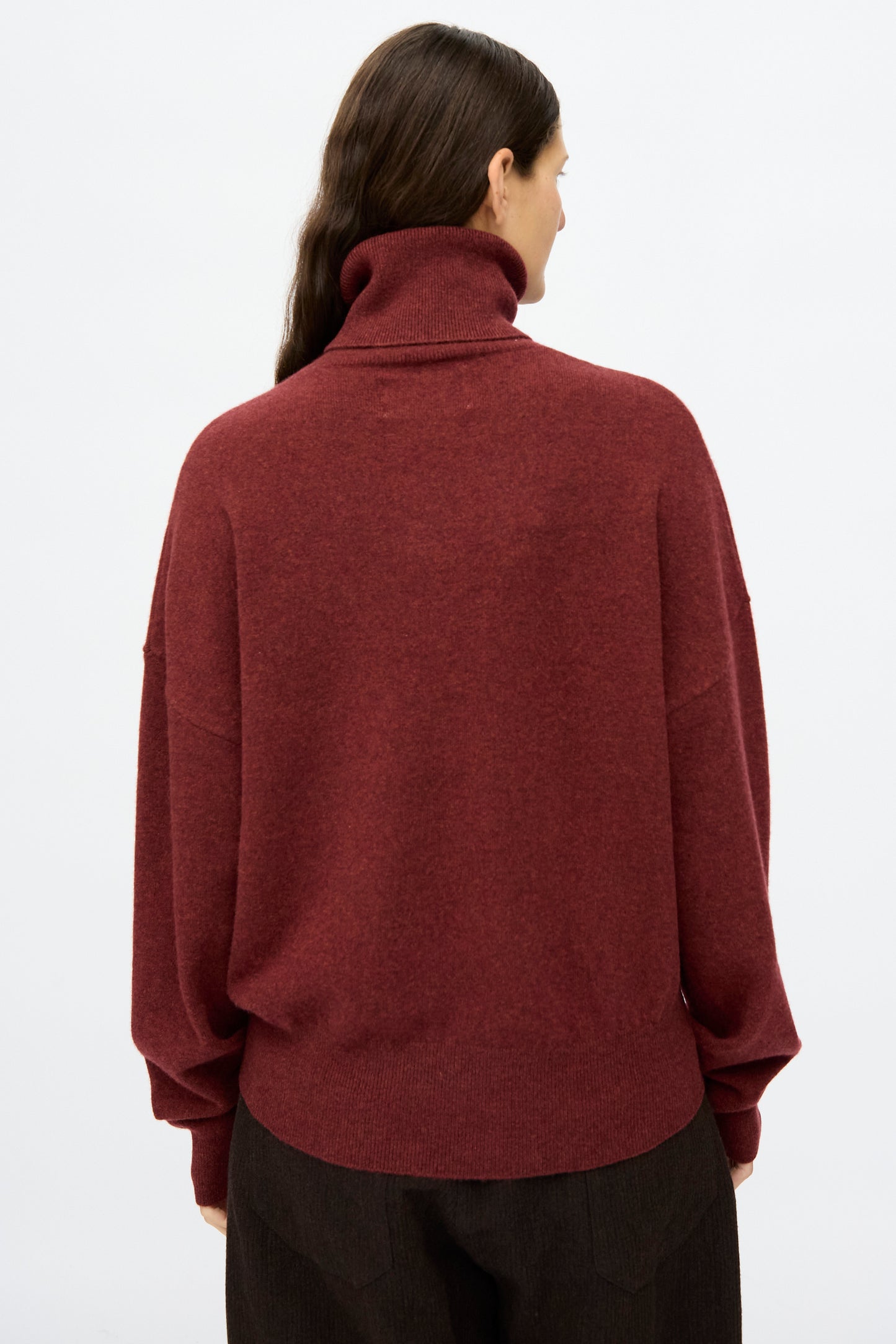 Person with long brown hair wears the No. 204 Jill Sweater in Maroon by Extreme Cashmere, a relaxed fit turtleneck, and dark pants, shown from the back against a plain white background.