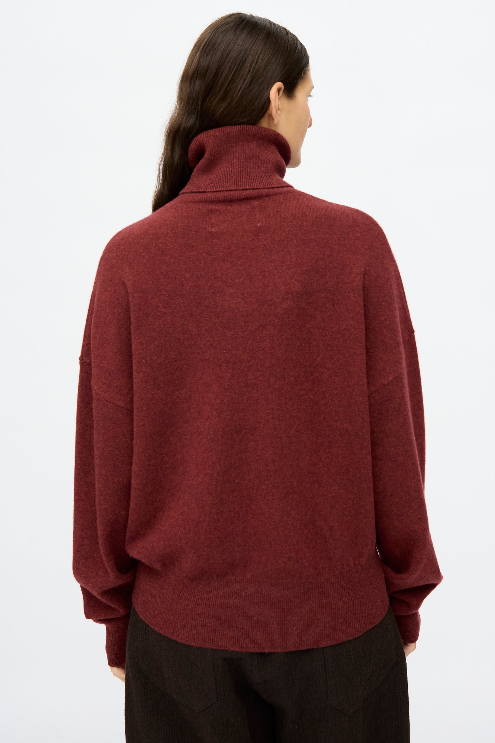 Person with long brown hair wears the No. 204 Jill Sweater in Maroon by Extreme Cashmere, a relaxed fit turtleneck, and dark pants, shown from the back against a plain white background.