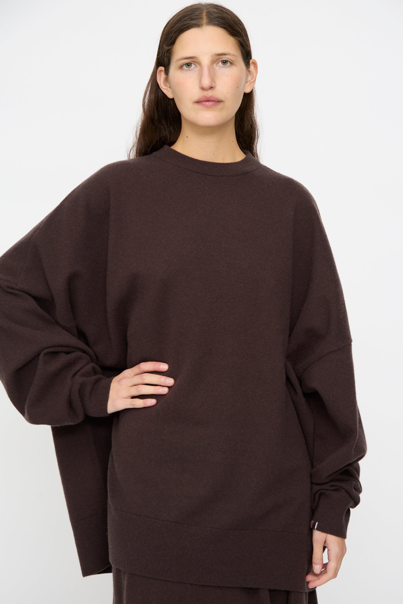 A person with long brown hair wears the Extreme Cashmere No. 246 Juna Sweater in Dark Brown and matching pants, standing against a plain white background.