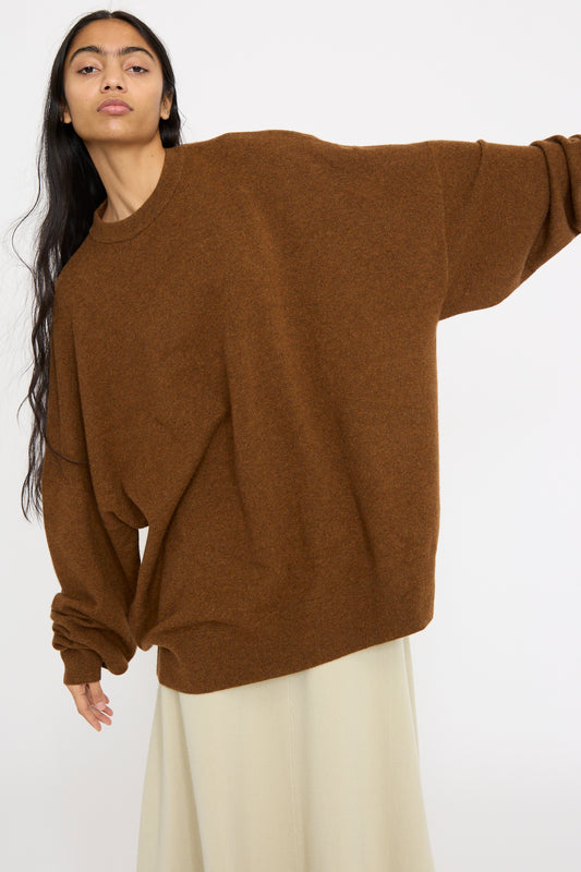 A model wearing Extreme Cashmere's No. 246 Juna Sweater in Rust paired with a cream skirt against a plain background.