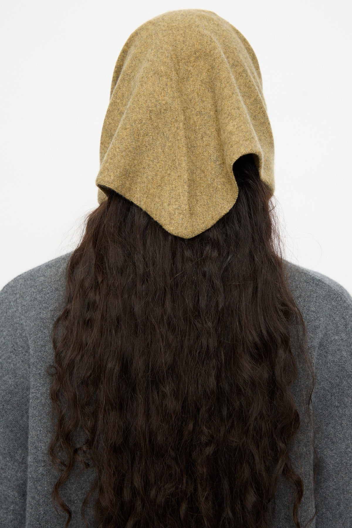 A person with long, wavy dark hair wearing a gray top and the Extreme Cashmere No. 35 Bandana in Hunter, styled as a triangle bandana, viewed from behind against a plain white background.