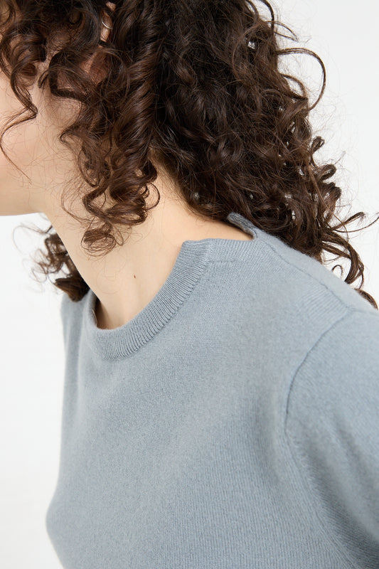 The woman is wearing a No. 36 Be Classic Sweater in Sage by Extreme Cashmere in a relaxed fit, showcasing her curly hair.