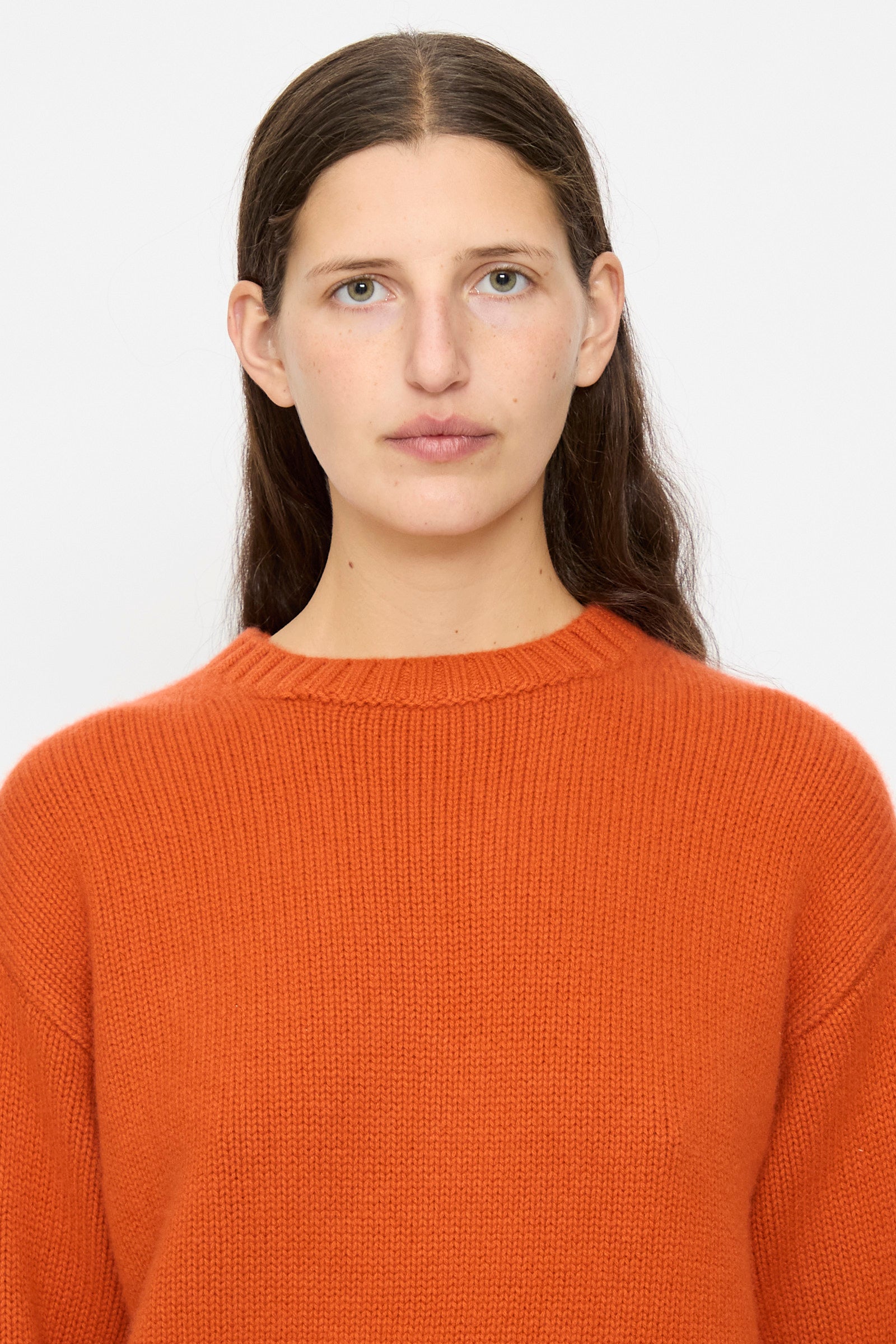 A person with long brown hair wears the Extreme Cashmere No. 373 Oldie Sweater in Dark Orange, styled in a relaxed fit, and looks directly at the camera against a plain white background.