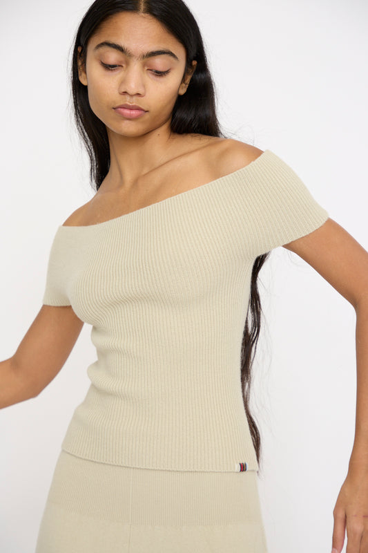 A person with long dark hair is wearing a slim-fit No. 381 Libra Sweater in Desert by Extreme Cashmere, crafted from cashmere rib knit, and gazes down slightly against a plain white background.