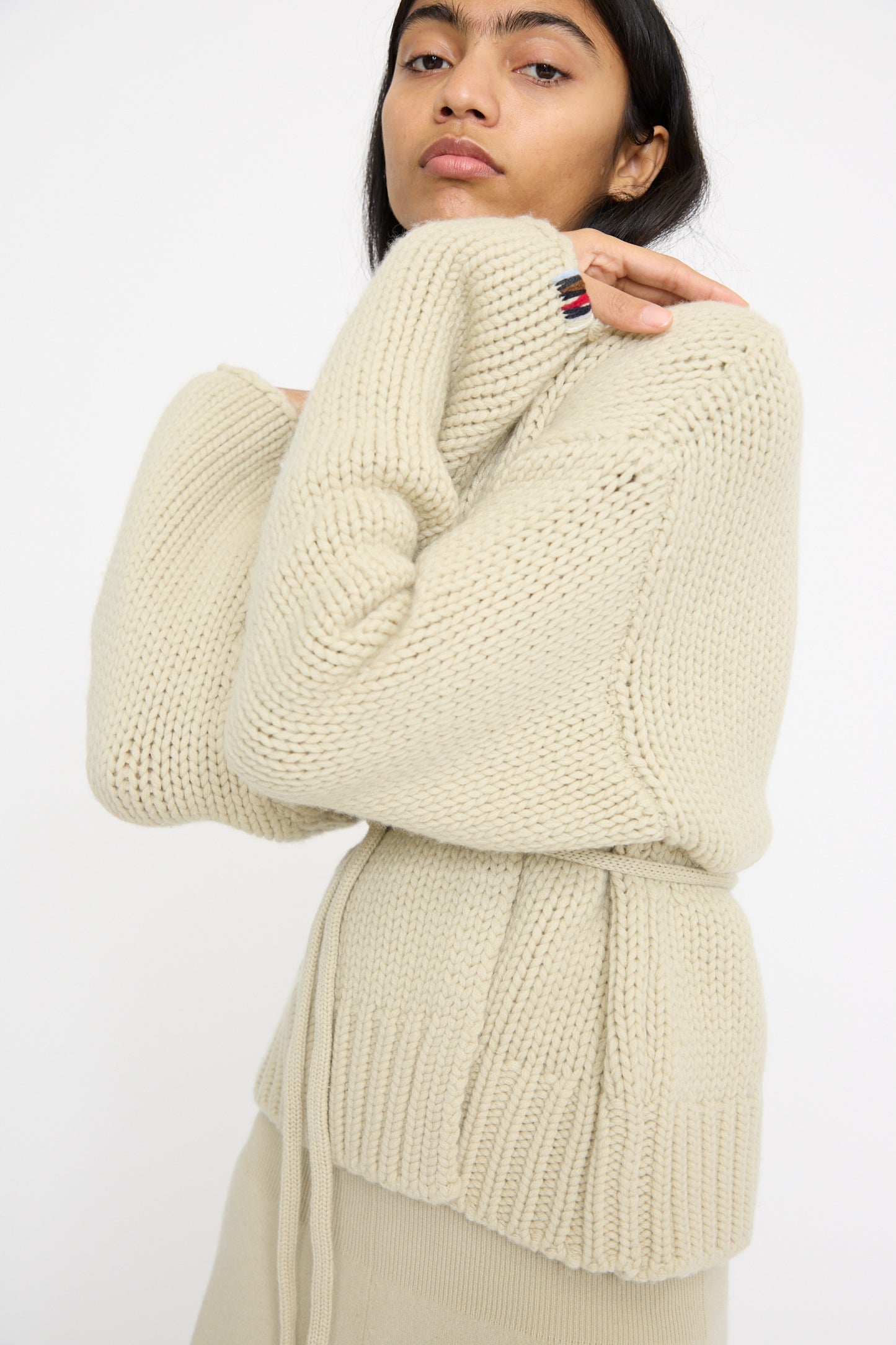 A person elegantly stands against a plain white background wearing the No. 384 Ginza Handknit Cardigan in Desert by Extreme Cashmere.