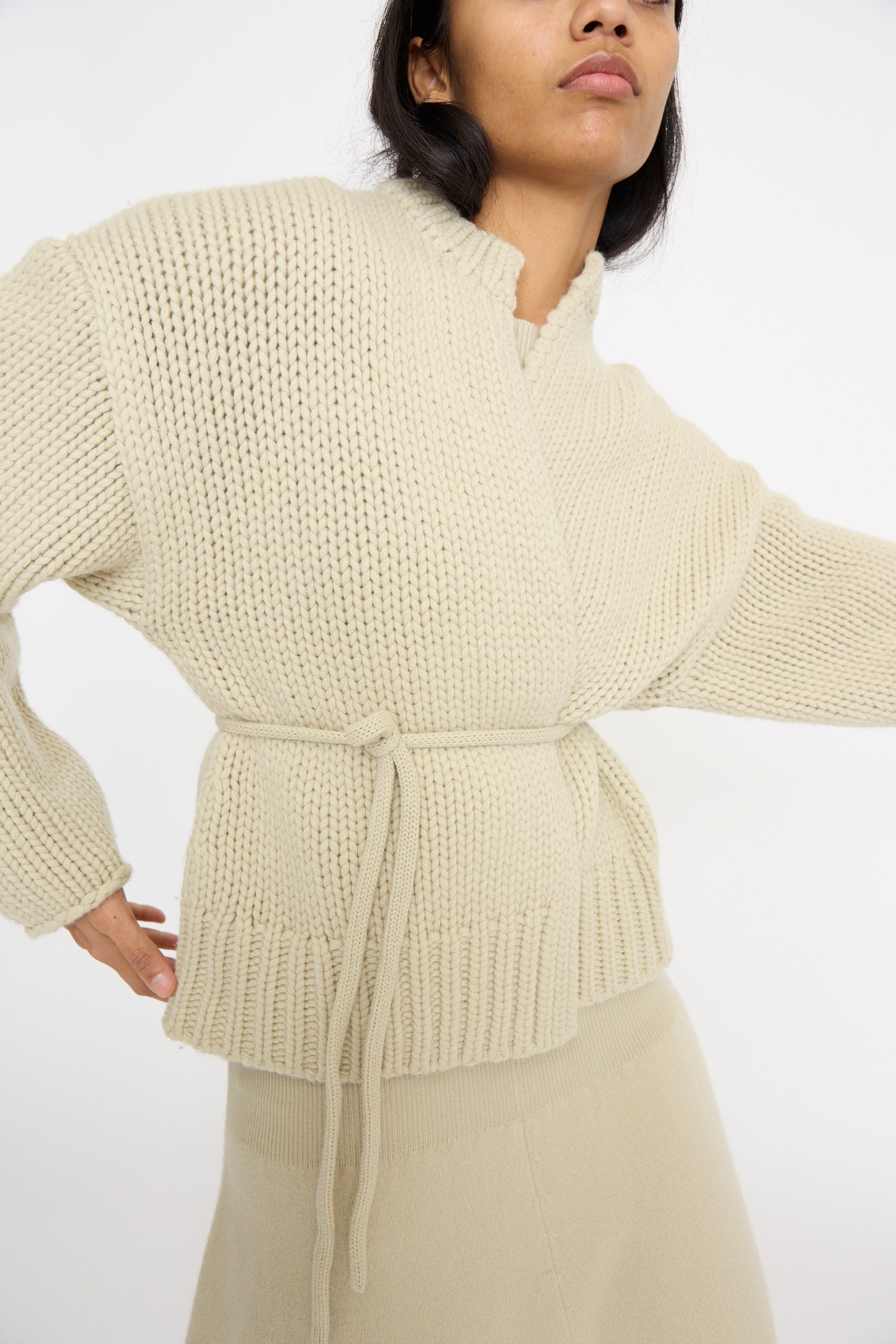 A person is wearing the No. 384 Ginza Handknit Cardigan in Desert by Extreme Cashmere, paired with a matching skirt against a white background.