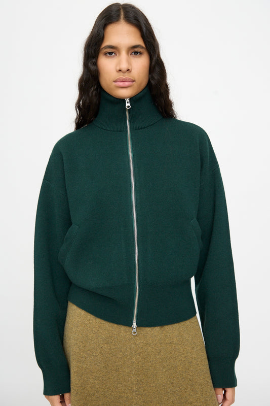 A person wearing the Extreme Cashmere No. 385 Xtra Cute Cardigan in Forest, styled with a brown skirt, stands against a plain light background.