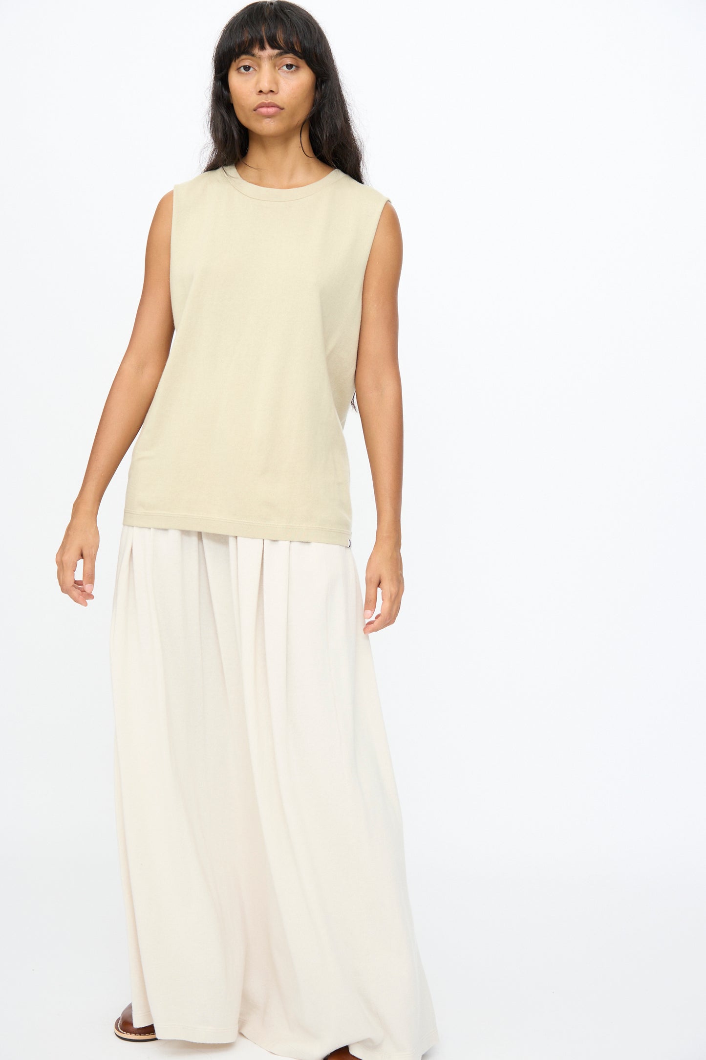 A person stands against a white background wearing Extreme Cashmere's No. 408 Muscle Tee in Desert and wide-legged, light-colored pants.