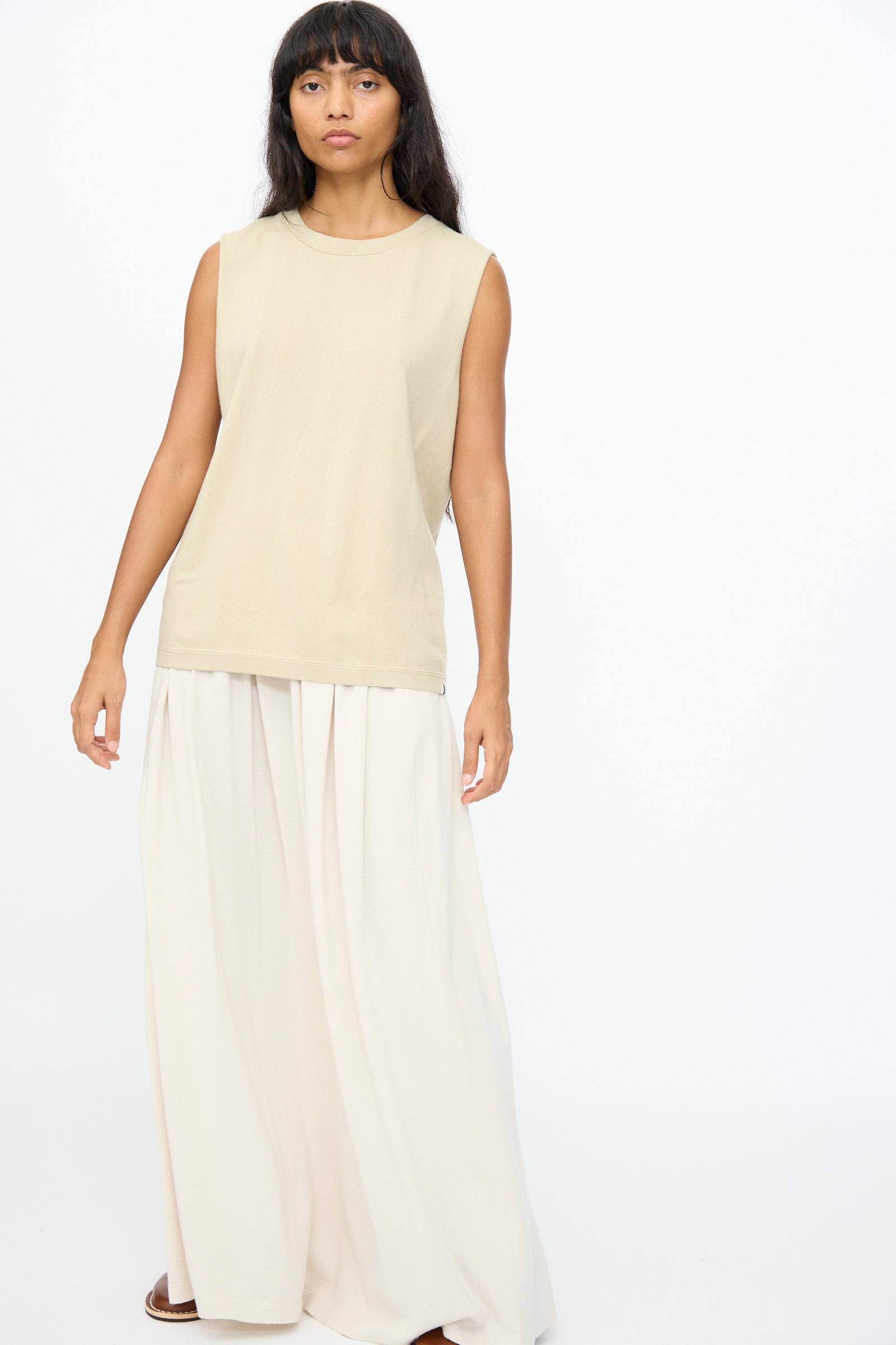 A person stands against a white background wearing Extreme Cashmere's No. 408 Muscle Tee in Desert and wide-legged, light-colored pants.