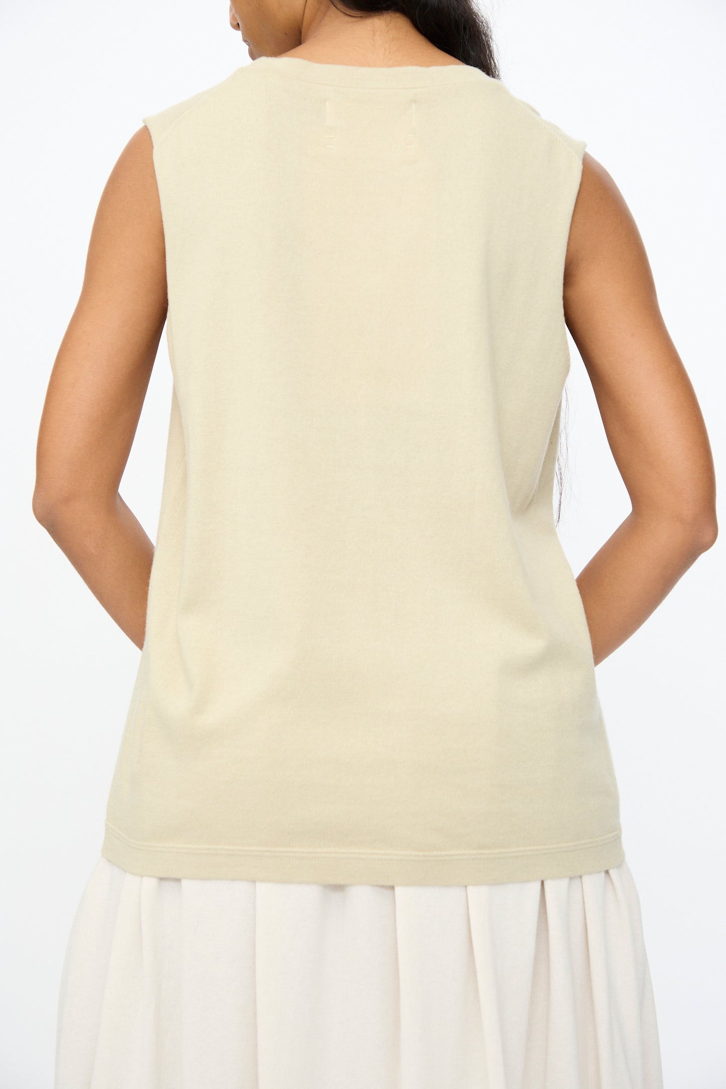 A person is shown from behind wearing the Extreme Cashmere No. 408 Muscle Tee in Desert, a sleeveless unisex cotton-cashmere blend, paired with a light skirt against a plain white background.