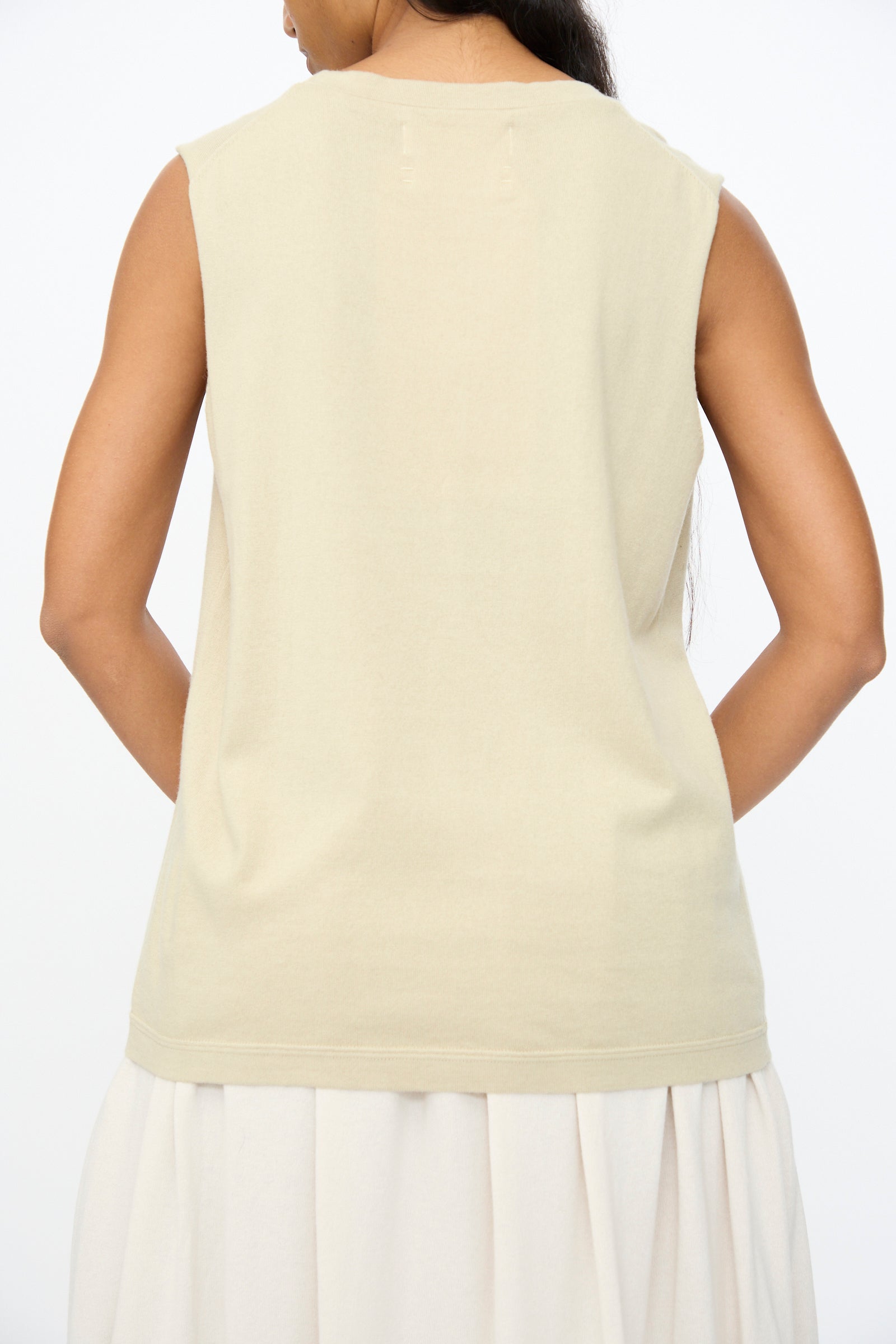 A person is shown from behind wearing the Extreme Cashmere No. 408 Muscle Tee in Desert, a sleeveless unisex cotton-cashmere blend, paired with a light skirt against a plain white background.