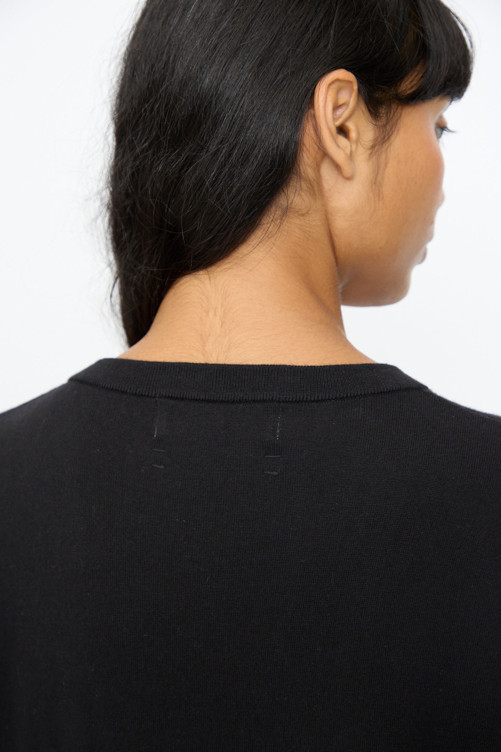 A person with long dark hair, seen from behind, wears the Extreme Cashmere No. 410 Inda Dress in Raven—a black maxi t-shirt dress featuring faint neckline stitching and a relaxed silhouette.
