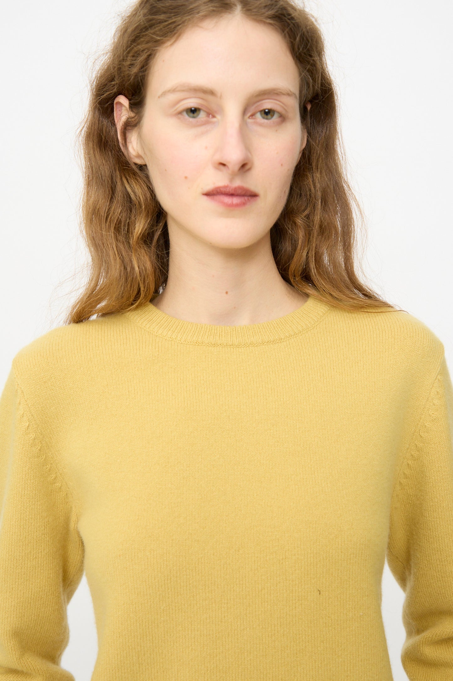 A person with long, wavy light brown hair wears the Extreme Cashmere No. 430 Sweater in Corn and looks directly at the camera against a plain white background.