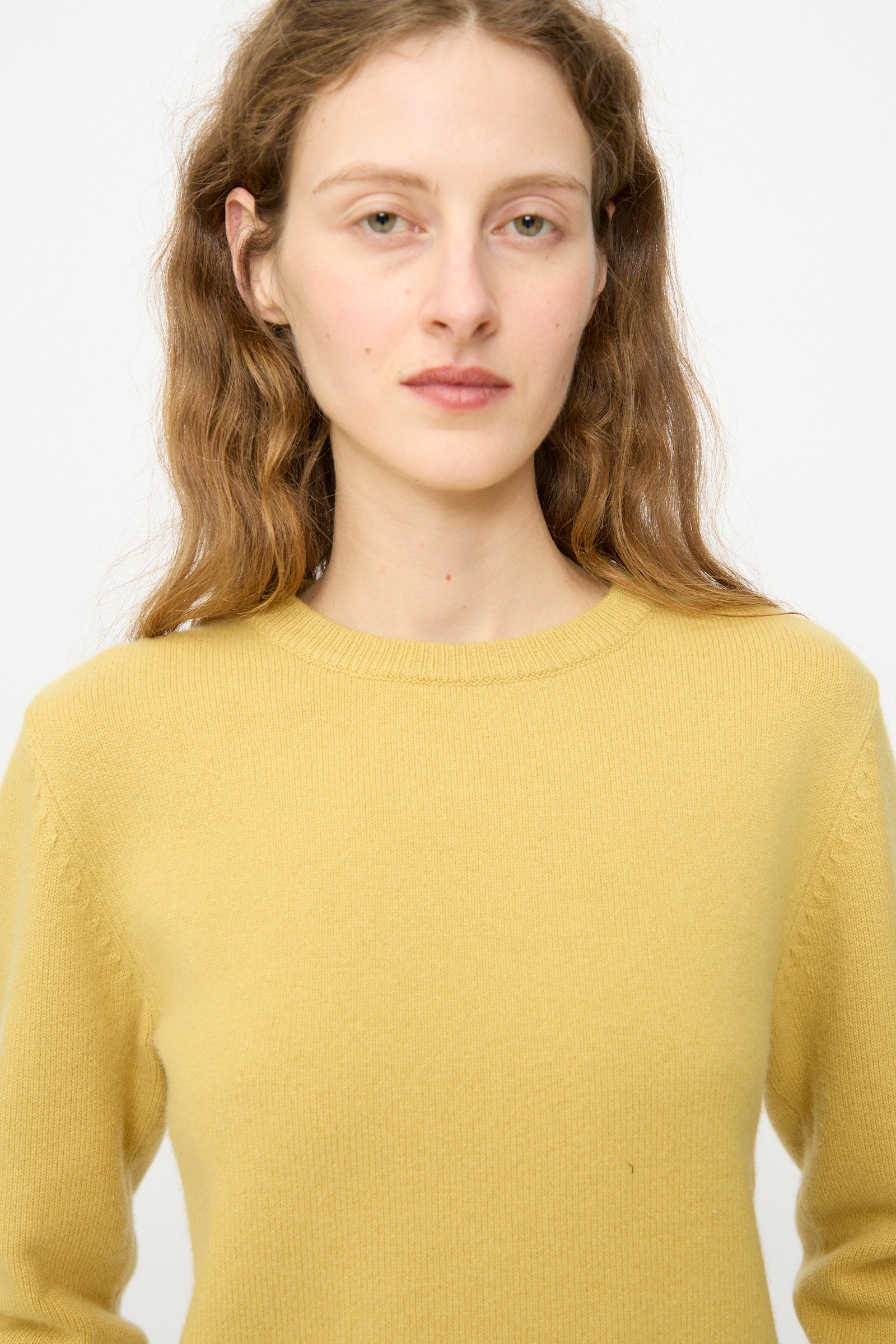 A person with long, wavy light brown hair wears the Extreme Cashmere No. 430 Sweater in Corn and looks directly at the camera against a plain white background.