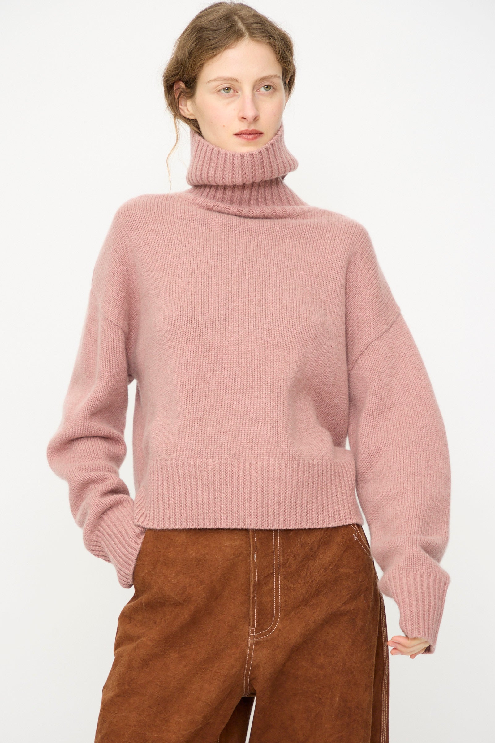 A person wears the Extreme Cashmere No. 434 Crop Xtra Sweater in Moor with brown pants, standing against a plain light background.