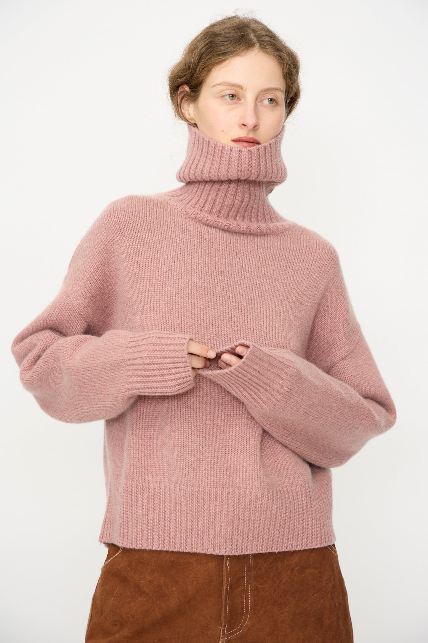 A person wears the No. 434 Crop Xtra Sweater in Moor by Extreme Cashmere paired with a brown skirt, standing against a plain white background.