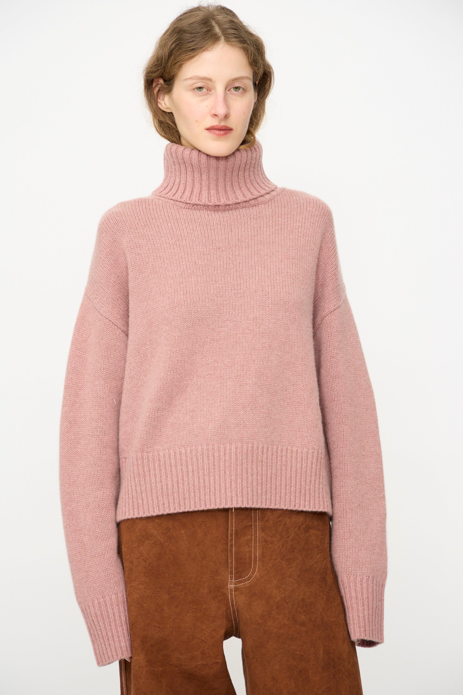 A person wears the Extreme Cashmere No. 434 Crop Xtra Sweater in Moor with brown pants, standing against a plain white background.