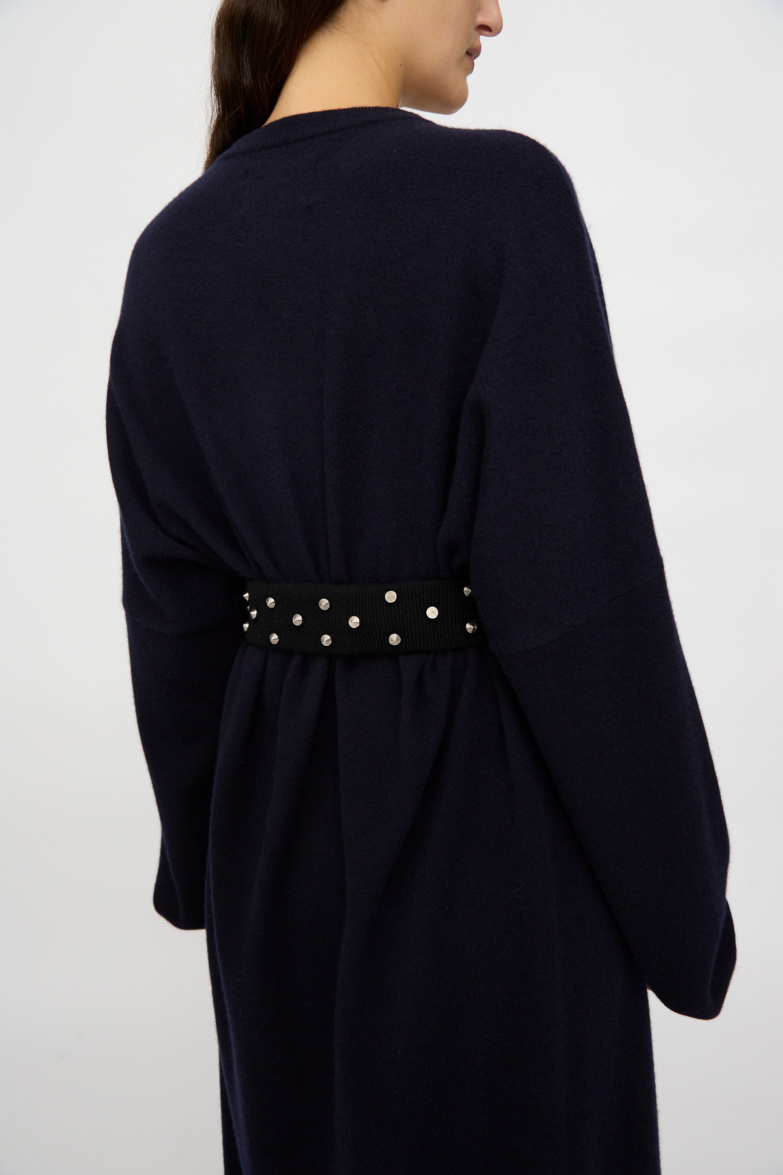 Photographed from behind against a plain background, a person wears a dark navy, long-sleeved coat styled with the Extreme Cashmere No. 446 Stud Belt at the waist.