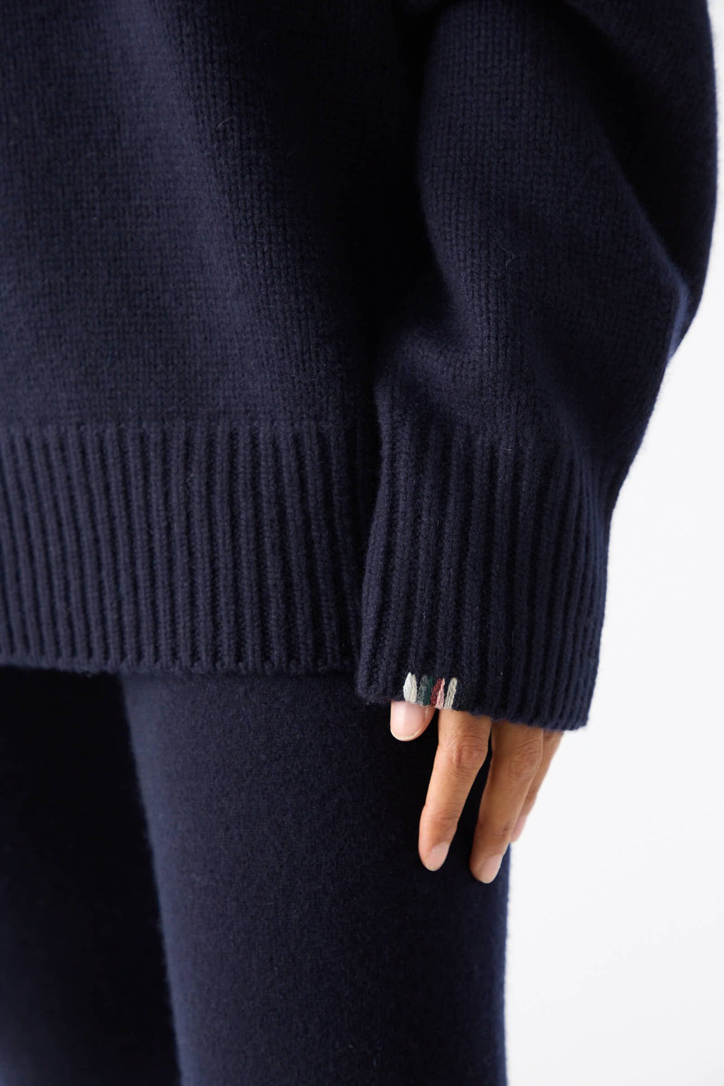 Close-up of a person wearing the No. 20 Oversize Extra Turtleneck Sweater in Navy by Extreme Cashmere, paired with matching pants, with a hand partially visible showing colorful threads peeking out from the sleeve cuff.