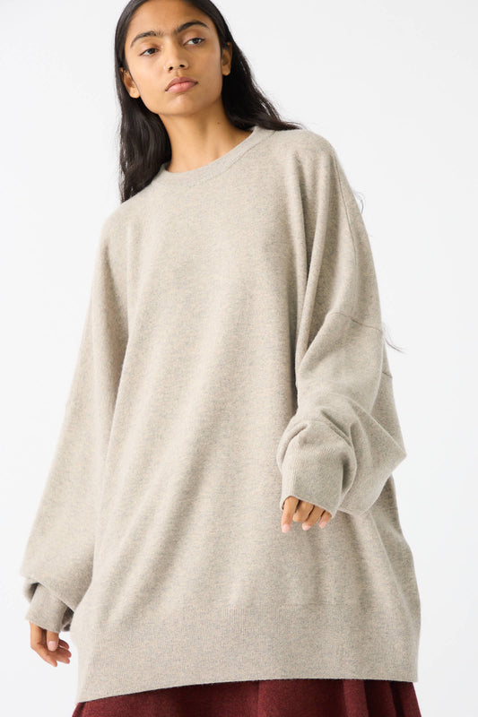 A person with long dark hair wearing the Extreme Cashmere No. 246 Juna Sweater in Moss and a maroon skirt stands against a plain white background.