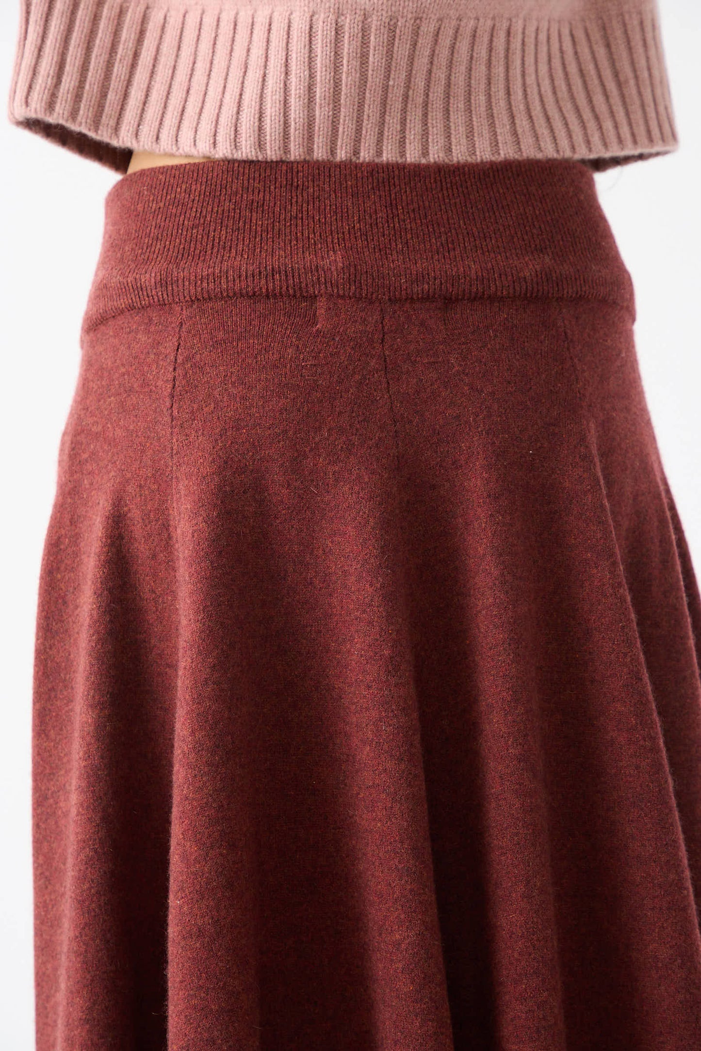 Close-up of a person wearing a ribbed, light pink knit sweater and the No. 313 Twirl Skirt in Maroon by Extreme Cashmere.