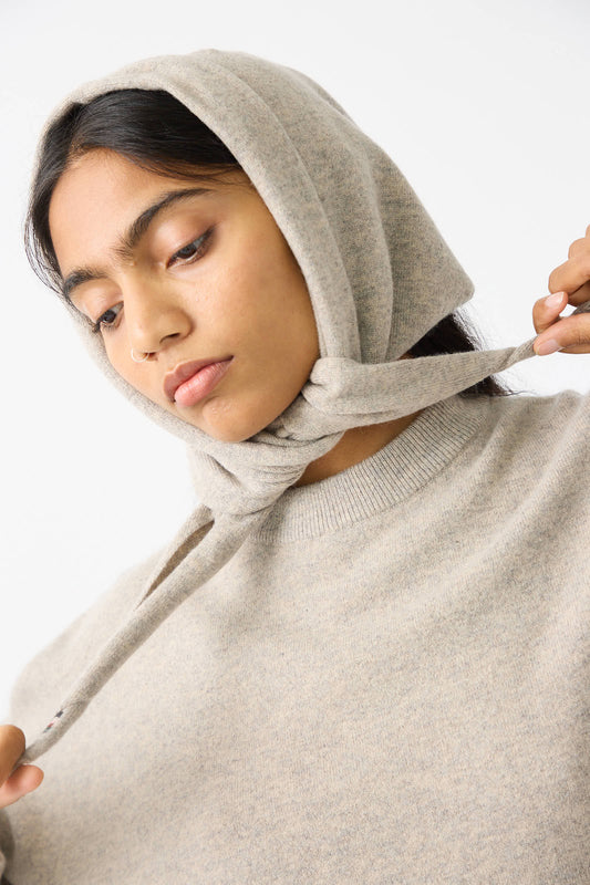 A person wearing Extreme Cashmere's No. 35 Bandana in Moss adjusts the hood strings while looking down.