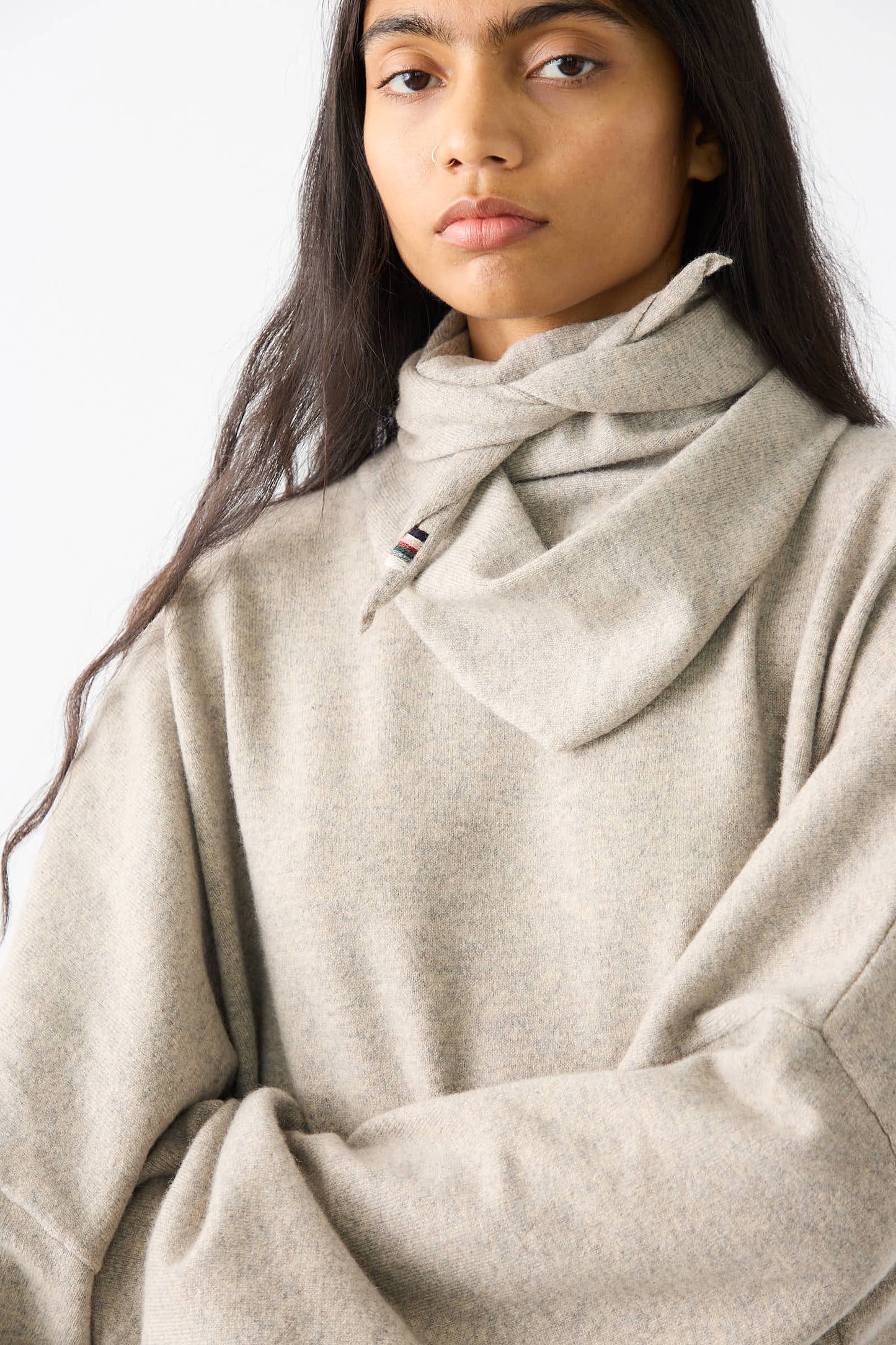 A person with long hair wears a high-neck, cashmere blend sweater in grey and a No. 35 Bandana in Moss from Extreme Cashmere, staring directly at the camera.