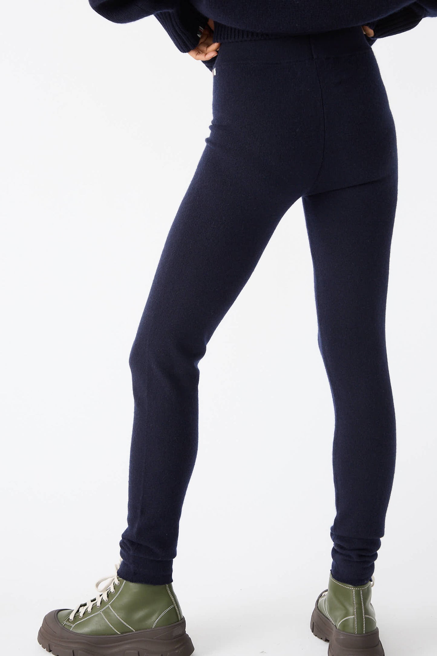 A person wearing the Extreme Cashmere No. 372 Beat Trouser in Navy with a rib-knit elasticated waist and green platform shoes stands with legs slightly apart against a white background.