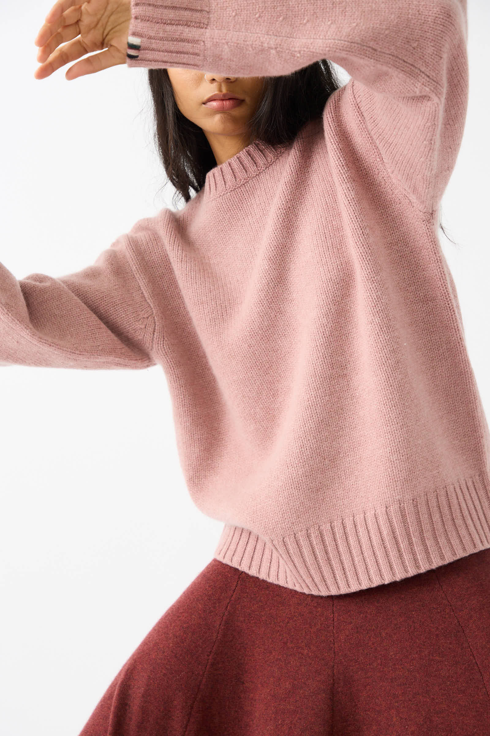 Person wearing an Extreme Cashmere No. 373 Oldie Sweater in Moor paired with a red skirt, arms raised and face partly obscured.