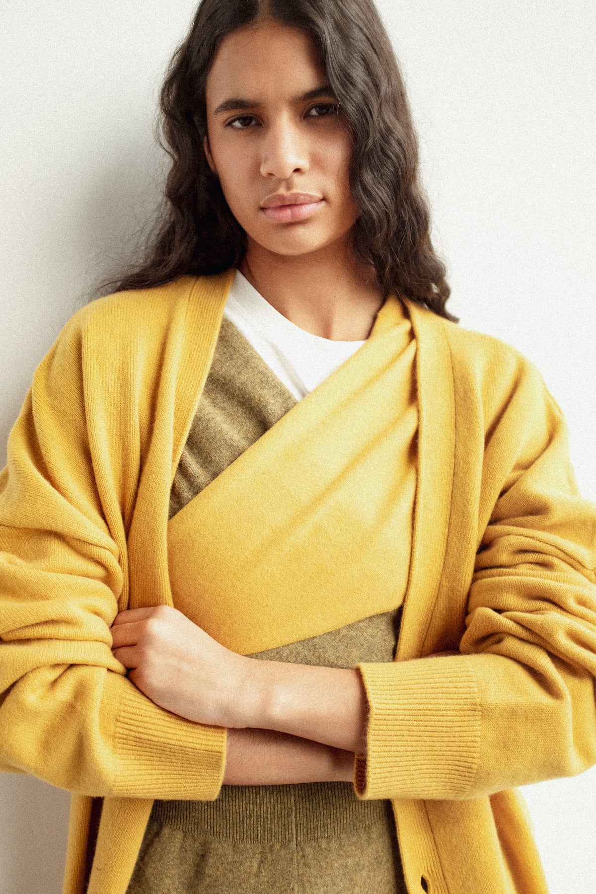 A woman crossing her arms wearing Extreme Cashmere's bandana's across her chest and the No. 517 Simo Cardigan in Wheat, against a white background.