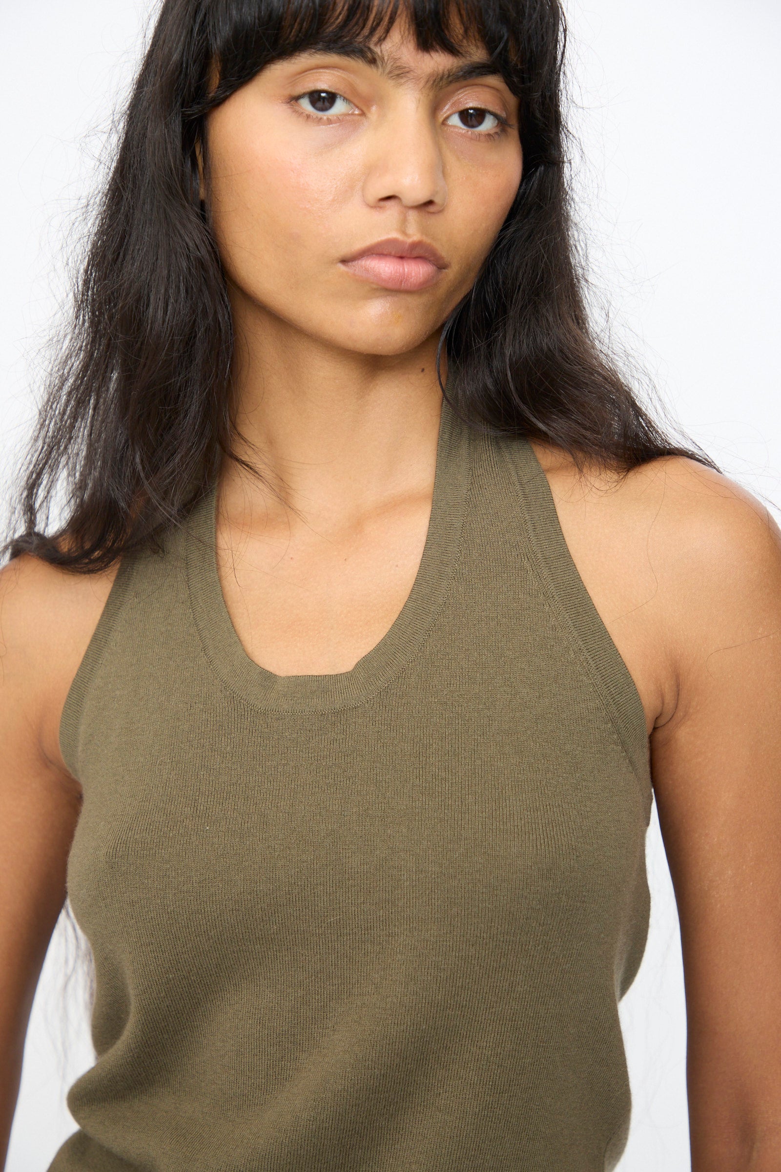 A woman with long dark hair models the Extreme Cashmere No. 409 Jerry Top in Army, a sleeveless scoop neck style, against a plain white background.