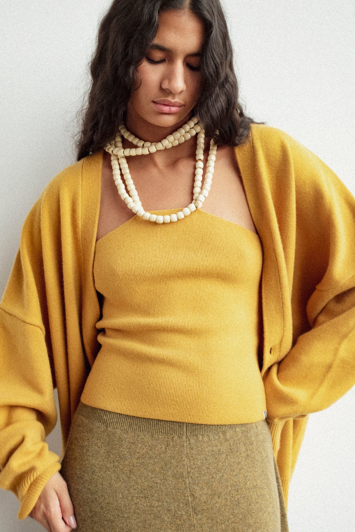 A woman looking down wearing Extreme Cashmere's No. 519 Candy Top in Wheat against a white backgroud.