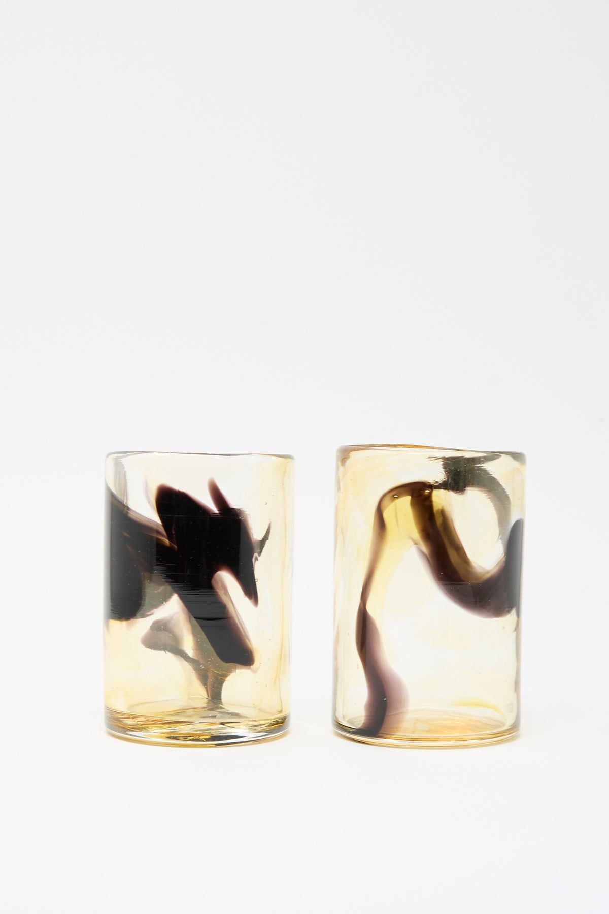 Two Hand Dyed Fumé glass tumblers featuring amber-toned glass with swirling black smoke-like patterns.