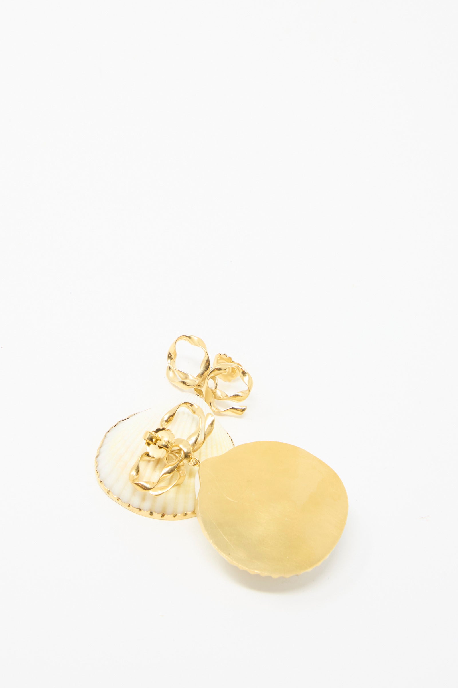 Grainne Morton's Bow and Shell Earrings, featuring 18k gold-plated silver, are showcased on a pristine white surface. One earring shows it's golden back. 