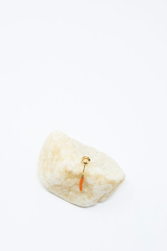 The Detachable Drop Earring in Coral by Grainne Morton is a small 18K gold plated earring with an orange pendant, handmade in Edinburgh and displayed on a light-colored stone against a white background.