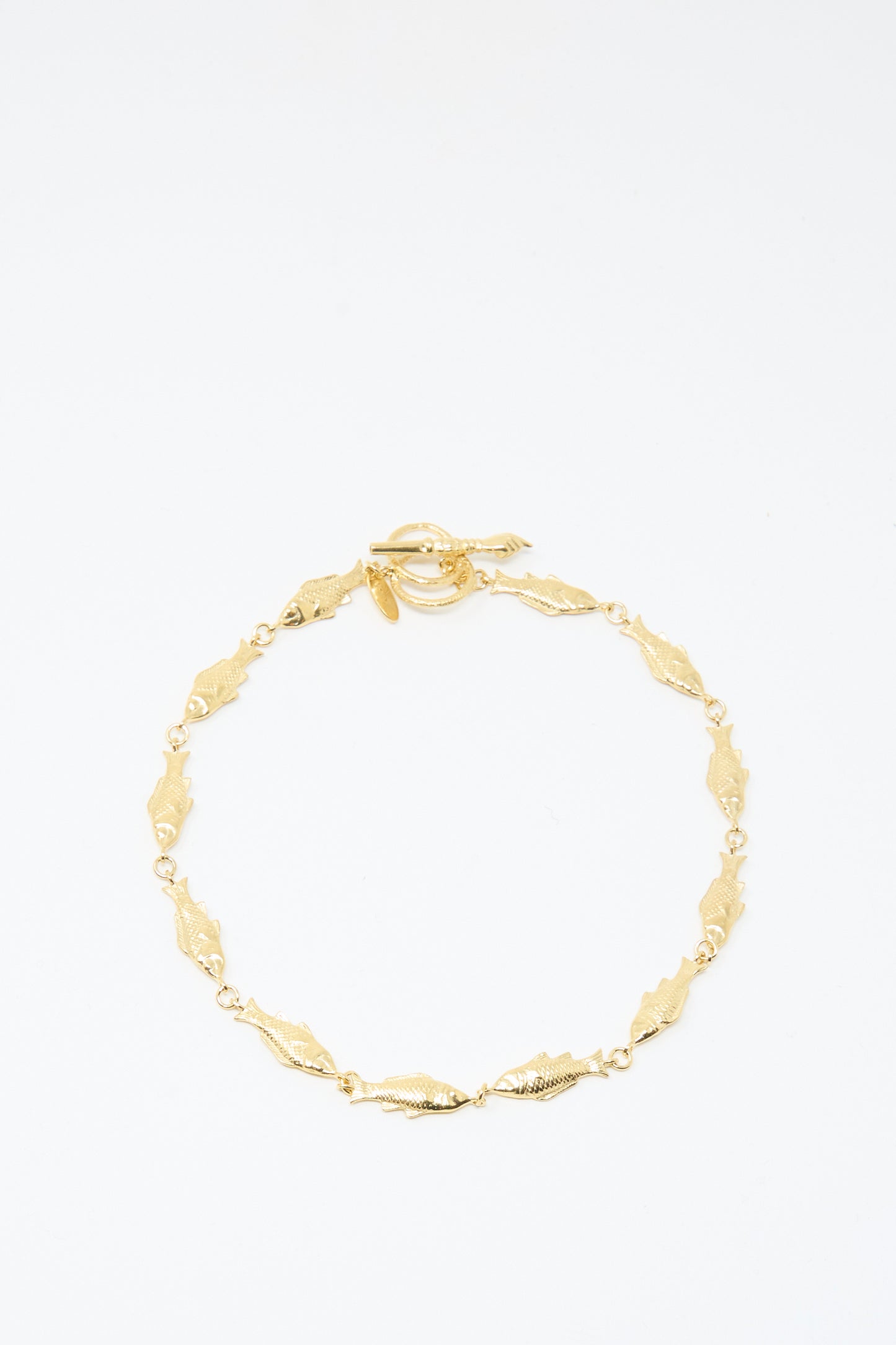 A Fish Necklace by Grainne Morton, featuring gold-plated silver with small leaf-shaped links and a circular toggle clasp, handmade in Edinburgh and shown on a plain white background.