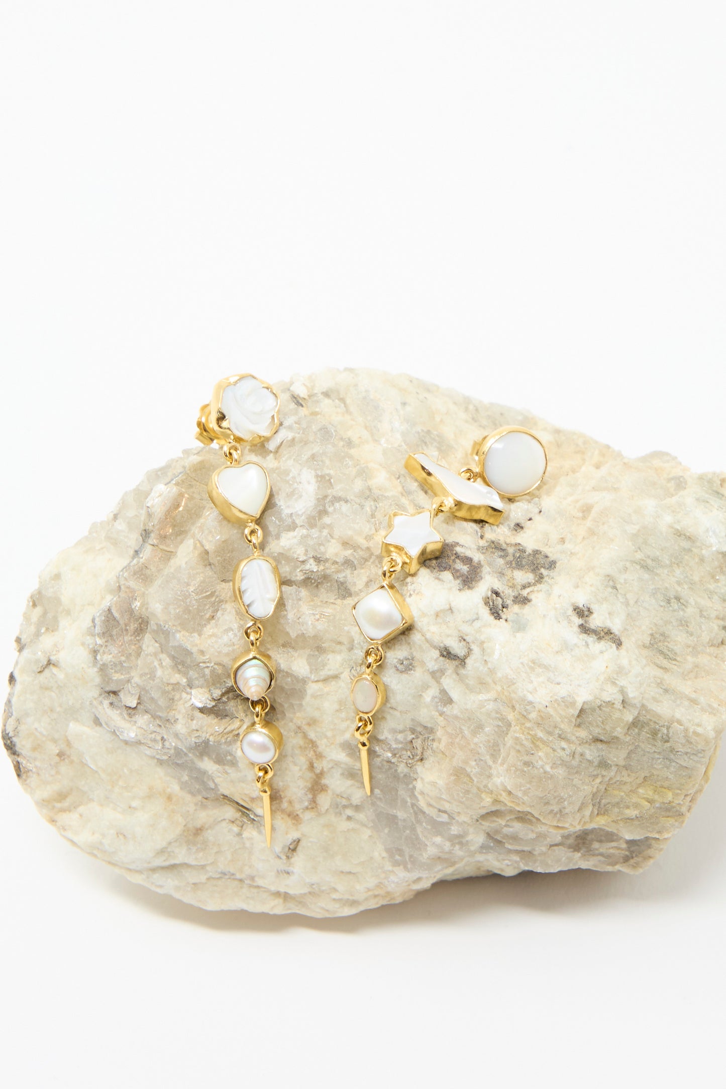 Five Charm with Victorian Drop Earrings by Grainne Morton feature gold drop designs with pearl and geometric charms. Made in Edinburgh from 18k gold-plated silver, they're showcased on a textured rock background against a white backdrop. 