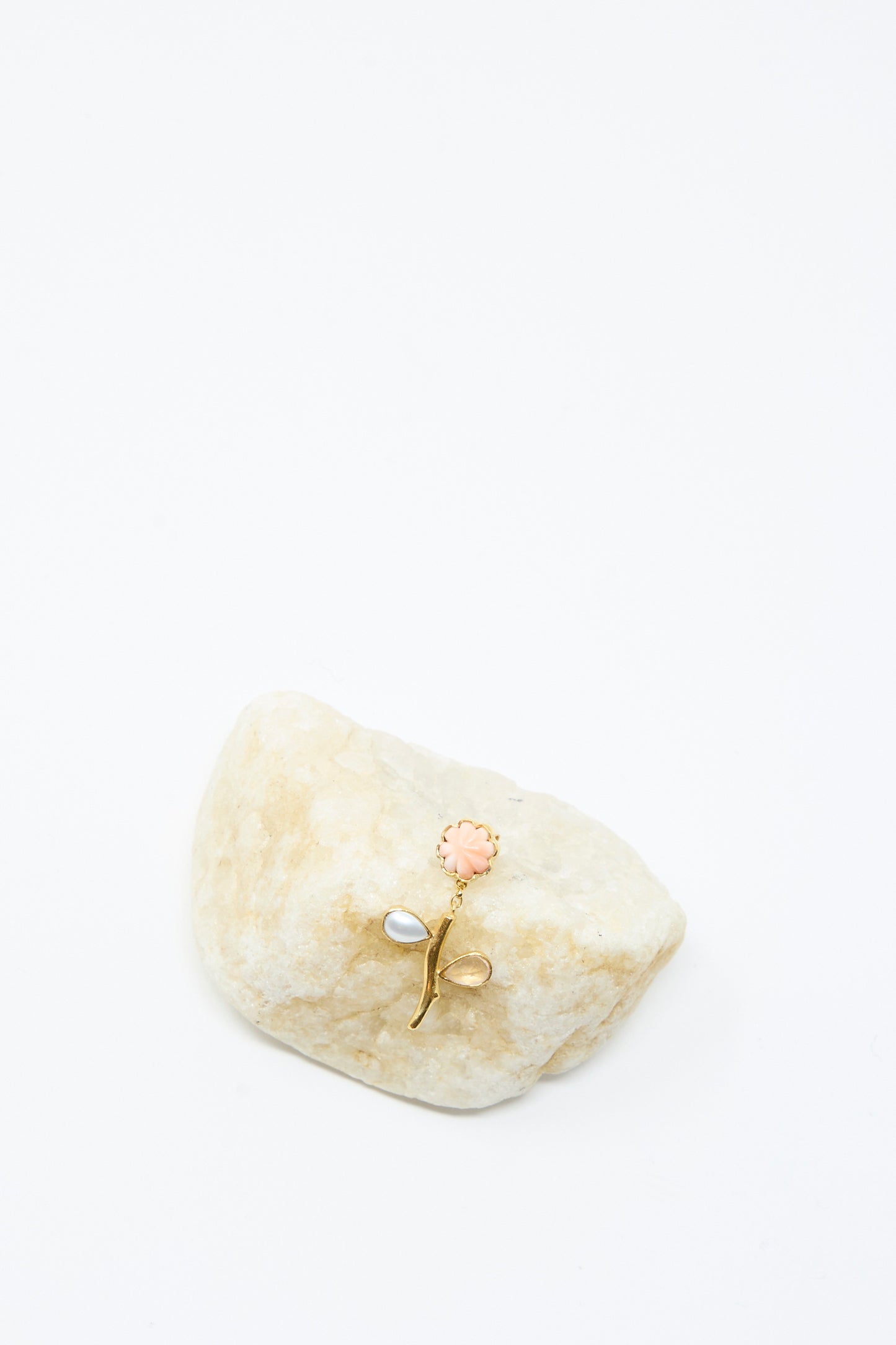 The Grainne Morton Flower Stem Drop Earring, featuring gold petals with pink and white accents, is displayed on a light stone against a white background.
