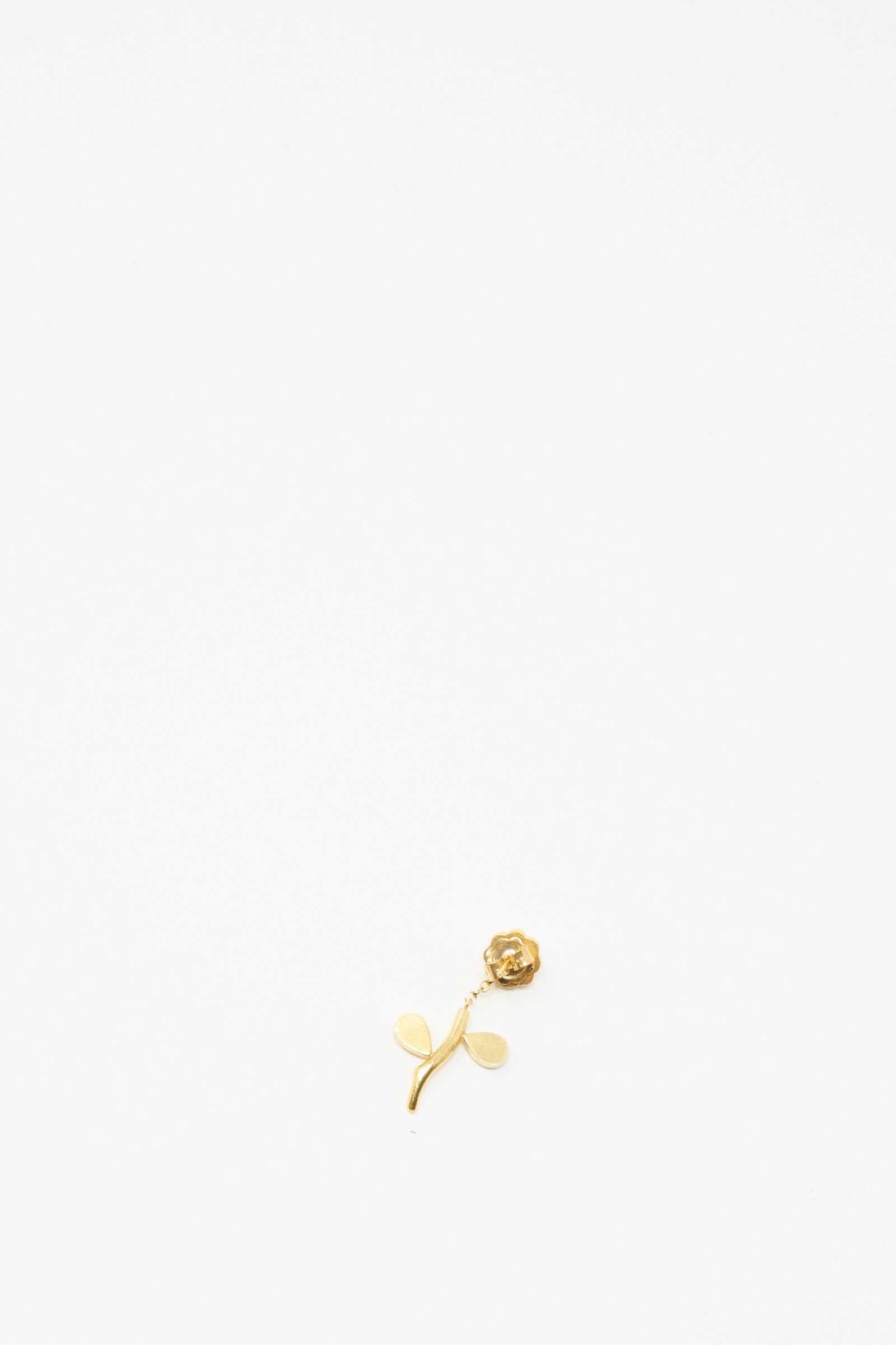 The Grainne Morton Flower Stem Drop Earring is a small gold rose-shaped piece with two leaves, displayed on a plain white background.