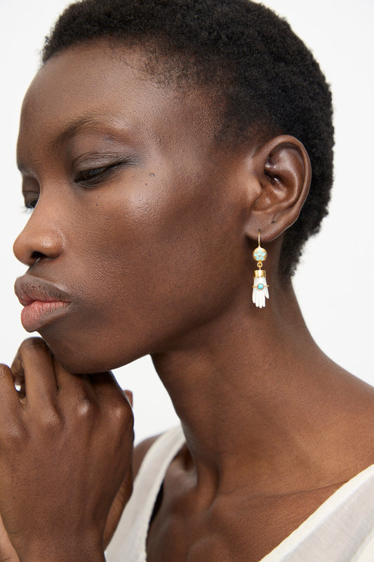 Close-up of a person with short hair wearing a white top and Grainne Morton’s Hand Hooks with Bracelet Earrings, 18K gold plated and hand-shaped, resting their chin on their hand.
