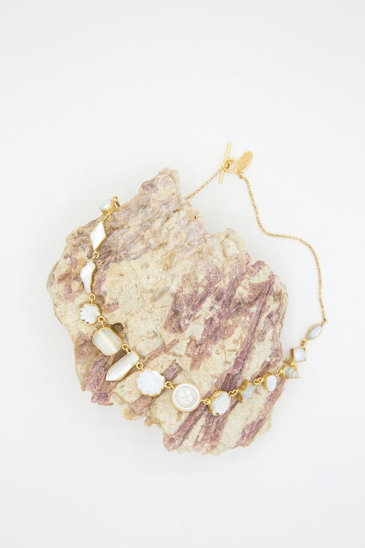A gold and Mother of Pearl charm necklace on a rock against a white surface.